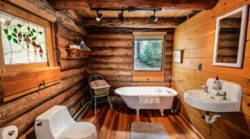A rustic log cabin bathroom that includes the most important fixtures: toilet, bathtub, and sink. 